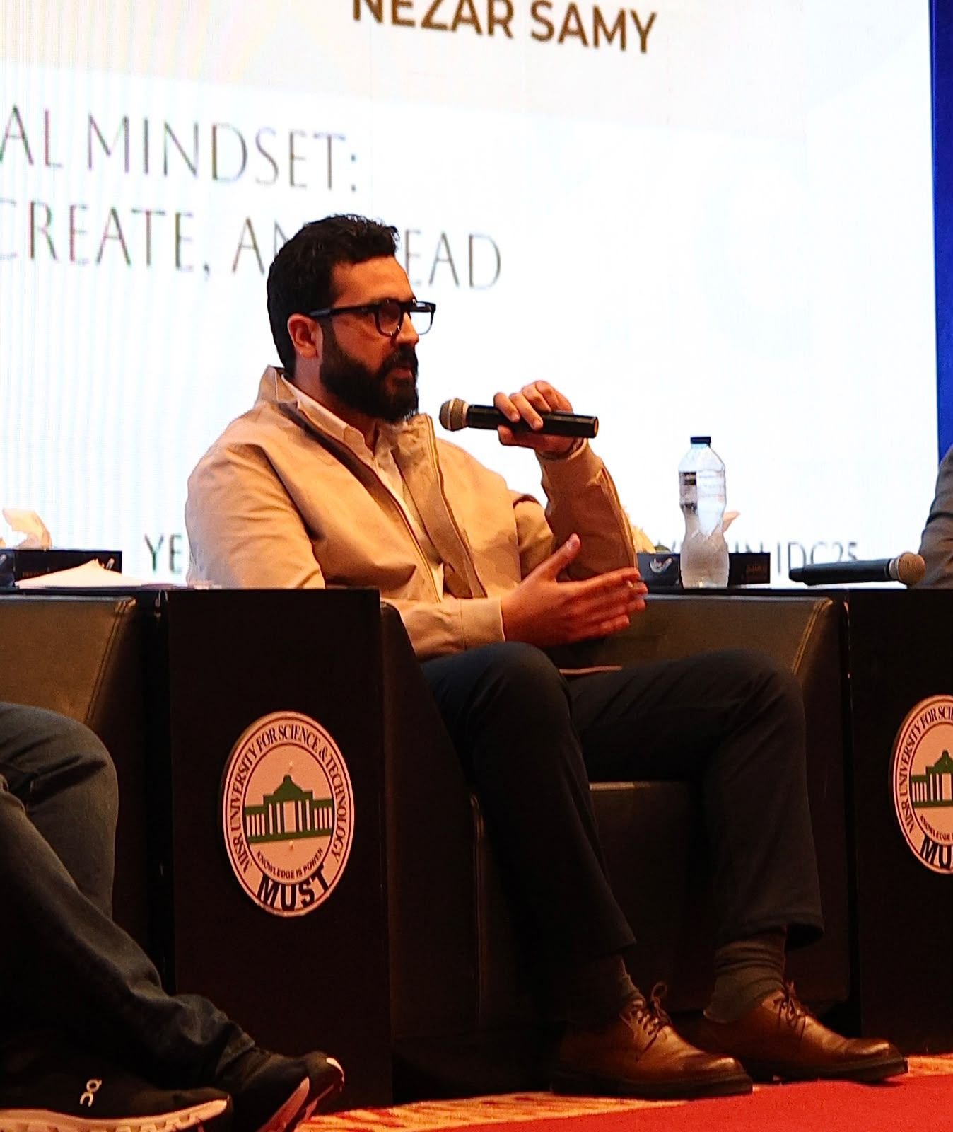 Eslam Toba speaking into a microphone on a panel stage at MUST