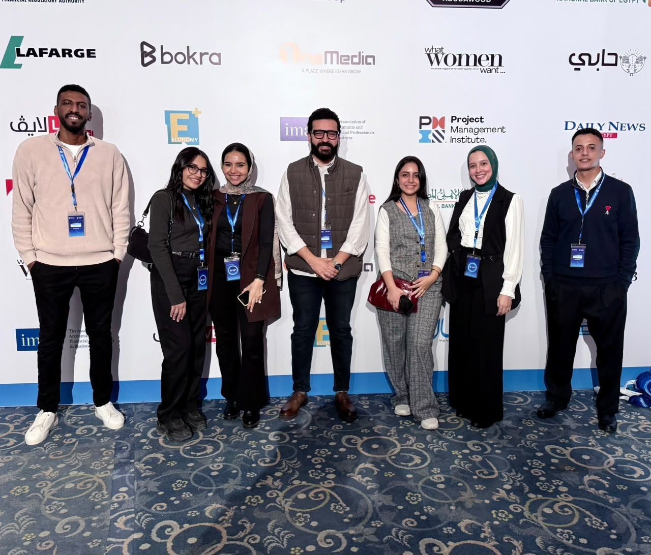 Eslam standing with six team members wearing event lanyards in front of a sponsor wall